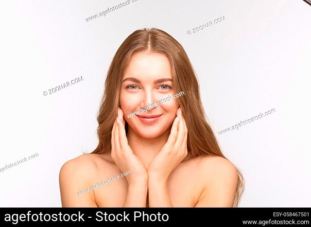 Closeup portrait of happy beautiful shirtless lady touching her face with both hands, looking at camera and smiling over white background