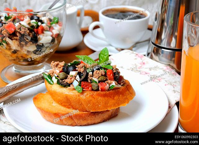 Breakfast from fried toast with chopped tuna with egg, cubes of tomatoes and olive slices, capers with a cup of coffee, a coffee pot on a tray
