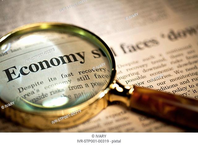 Looking at headline on financial page of newspaper through magnifying glass