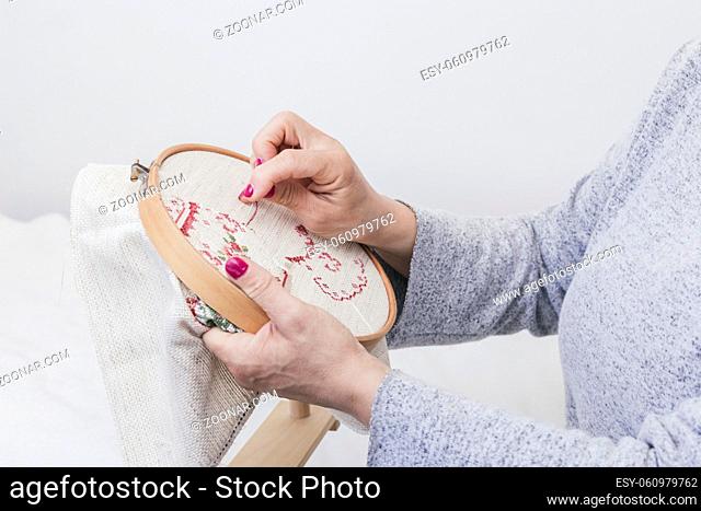 (1)woman s hand cross stitching pattern on a hoop against white background