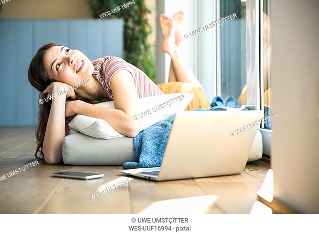 Relaxed young woman lying at the window at home with laptop