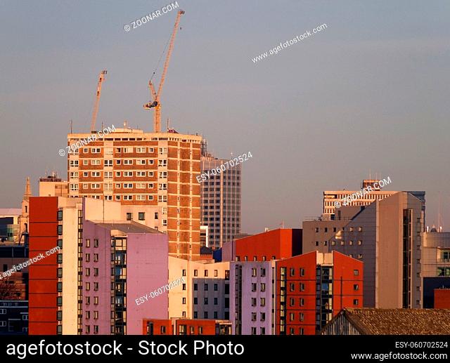 a cityscape view of tall modern residential developments in leeds city centre with a construction crane working on new developments with a bright blue sunlit...