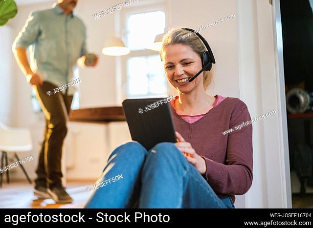 Happy freelancer wearing headset working on tablet PC at home office