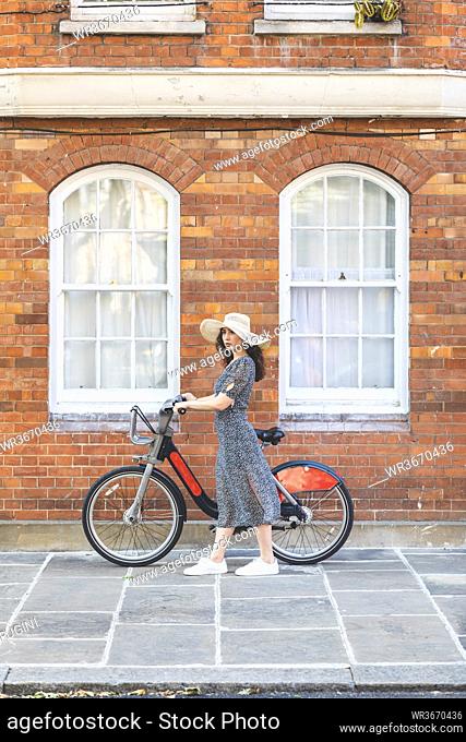Young woman wearing hat with bicycle standing on street in city