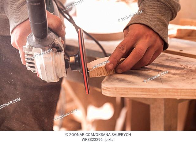 Worker polishing wood table where carpenter hands sanding a wood with electric sander