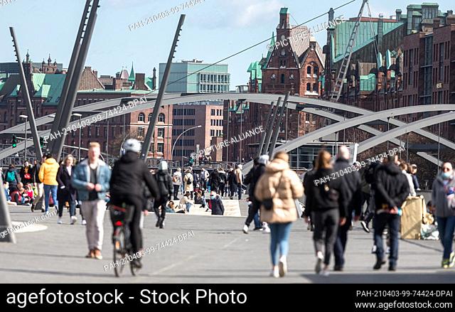 03 April 2021, Hamburg: Excursionists stroll along Baumwall against the backdrop of the historic Speicherstadt on the flood protection system