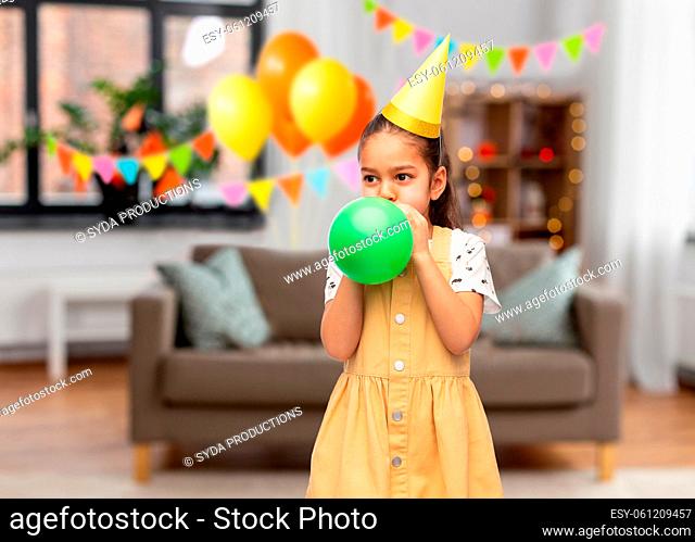 girl blowing balloon at birthday party at home