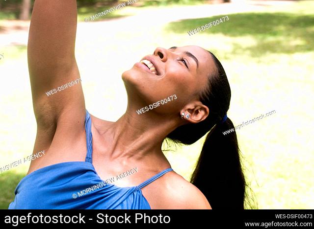 Smiling sportswoman with hand raised looking up while exercising during sunny day