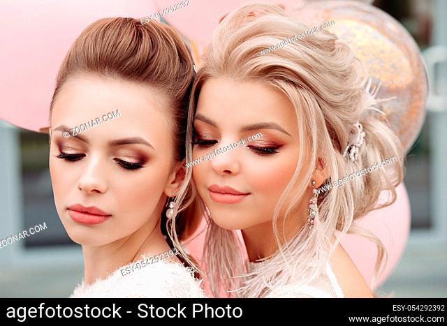 Portrait of attractive, stunning ladies with professional make up and hairstyles wearing white laced outlooks. Brunette and blonde looking down showing their...