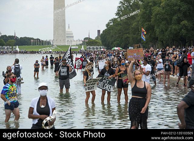 People stand in the cool water of the Reflecting Pool with their signs during the “Get Your Knee Off Our Necks” March on Washington at the Lincoln Memorial in...