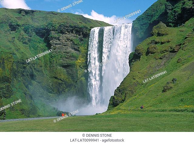 Skogarfoss waterfalls. Cascade of water. Cliffs. Figure in red coat
