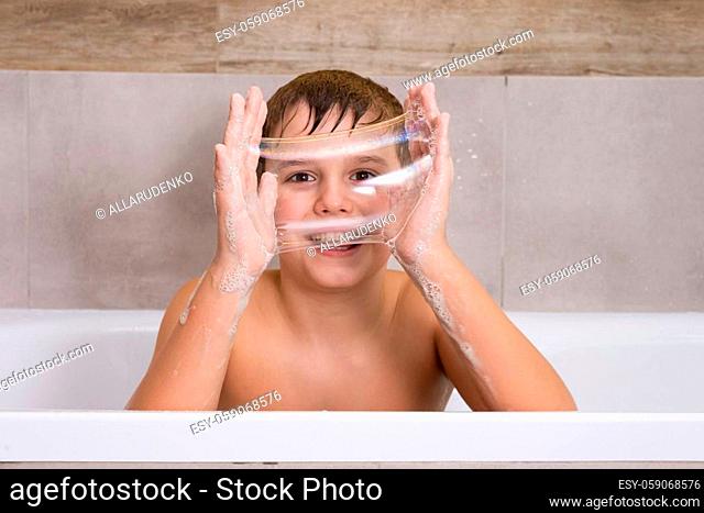 Portrait of funny boy playing with with soap shampoo or gel in bathroom Happy child bathe and inflates soap bubbles healthy childhood