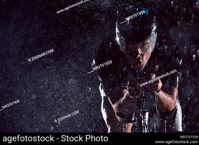 triathlon athlete riding professional racing bike fast at night with bad weather and falling rain