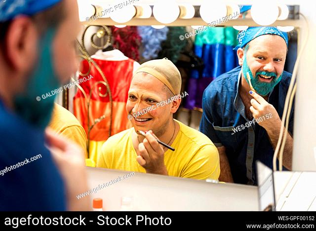 Smiling friends applying drag queen makeup on face at dressing room