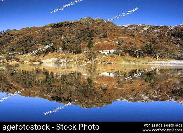 UK - England Northumberland Loughrigg Tarn Winter view over flat calm Loughrigg Tarn to fells and whitewashed farmhouse