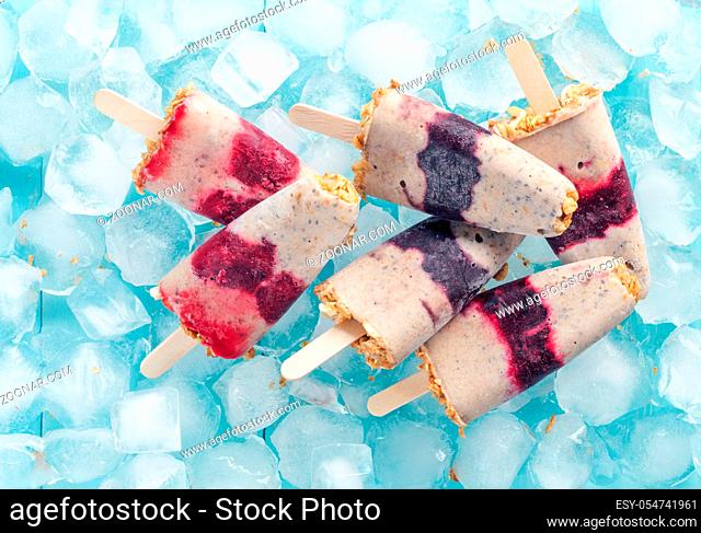 Homemade ice cream popsicle with berries, granola and chia seeds. Healthy summer breakfast concept. Popsicles from yogurt and banana with berries and granola