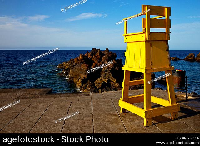 garbage basket yellow lifeguard chair cabin in lanzarote spain  rock stone sky cloud beach water musk pond coastline and summer