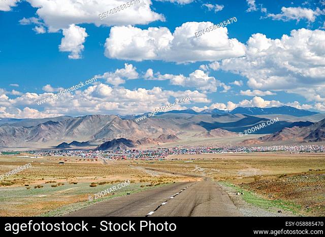 Empty Asphalt road in Mongolia with mongolian town Bayan-Olgii (Bayan-Ulgii or Ulgii) on background under blue sky