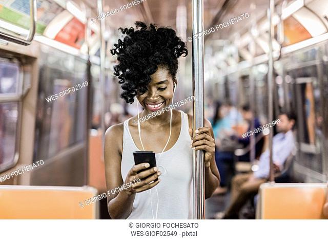 USA, New York City, Manhattan, portrait of happy woman looking at cell phone in underground train