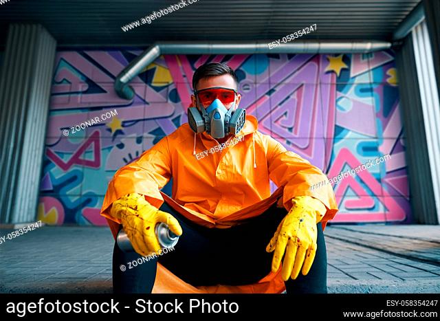Graffiti painter rest near the wall with his paintings looking to camera. Street art concept