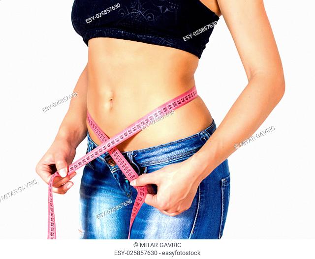 Slim Female with perfect healthy fitness body, measuring her thin waist with a tape measure. Caucasian young woman in jeans, over white background