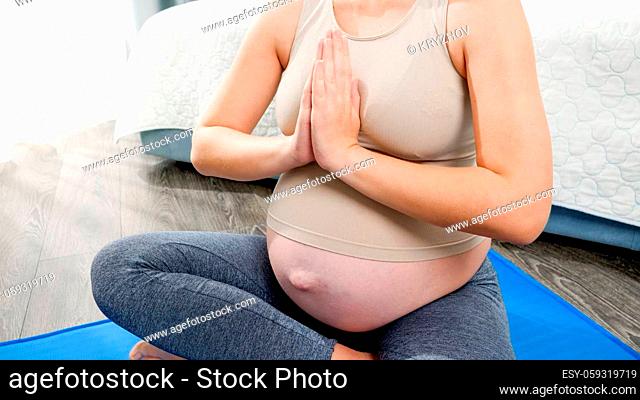 Closeup of pregnant woman meditating and relaxing on fitness mat at home. Concept of healthy lifestyle, healthcare and sports during pregnancy
