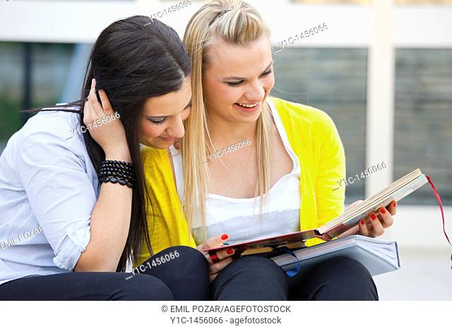 Attractive young women are sitting on low steps and looking at album photos
