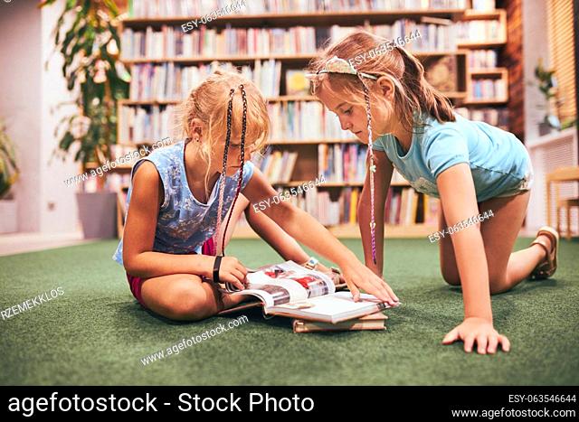Two schoolgirls reading books in school library. Primary school students learning from books. Pupils doing homework. Children having fun with books in school...
