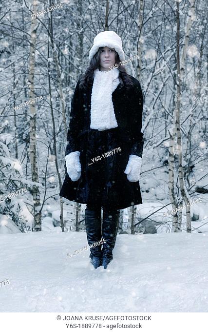 a woman in a black coat with a white hat and white scarf in the snow