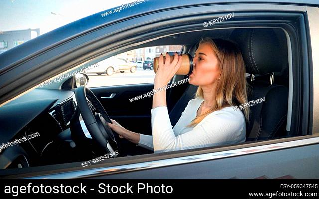 Portrait of beautiful young woman drinking coffee-to-go while driving a car at morning