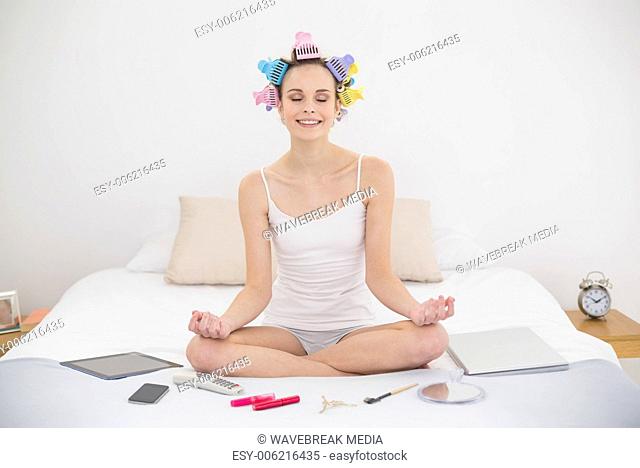 Relaxed natural brown haired woman in hair curlers meditating in lotus position