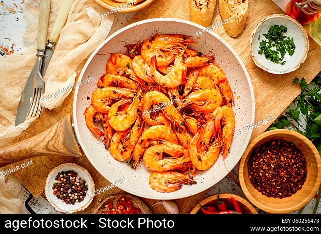 Roasted Prawns on frying pan served on white wooden cutting board. Rusty wooden background. Seafood lunch or dinner concept. Top view, flat lay