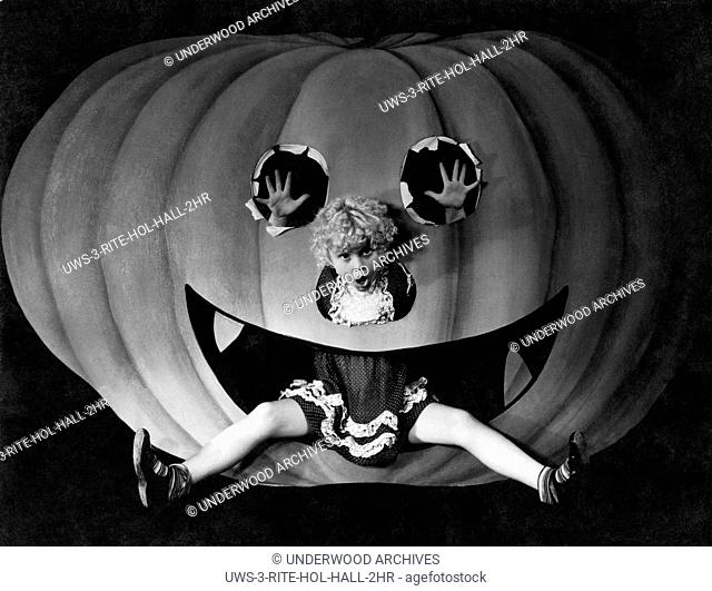 United States: c. 1927. A young girl in the mouth of a cut out pumpkin on Halloween