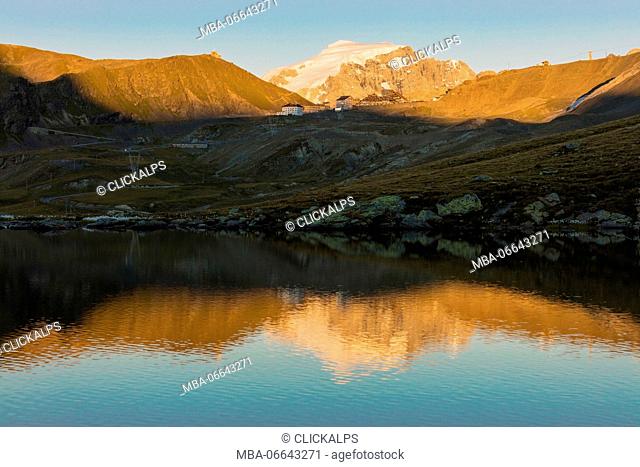 The rocky peaks are reflected in the alpine lake at sunset Stelvio Pass Valtellina Lombardy Italy Europe