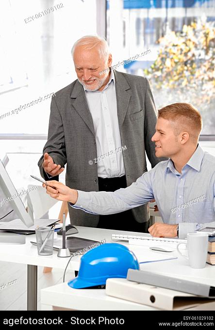 Young architect discussing work on computer screen with smiling senior boss