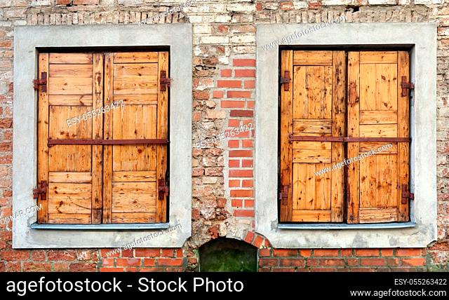 Two windows with closed locked wooden blings in the aged brick wall of a ruined house. Panoramic collage from several outdoor street photos