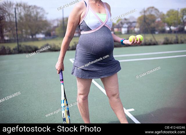 Pregnant woman in dress playing tennis on tennis court