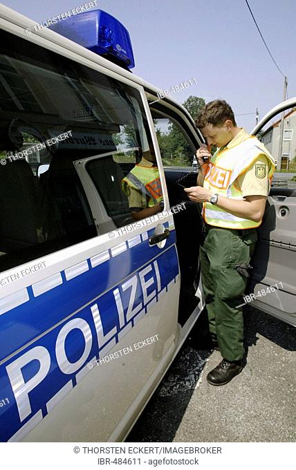 A german police officer standing beside his car talking in a radiophone, near the czechian boarder, Saxony, Germany