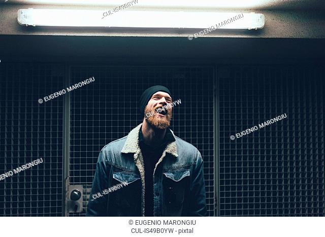Young male hipster laughing in dark city doorway at night