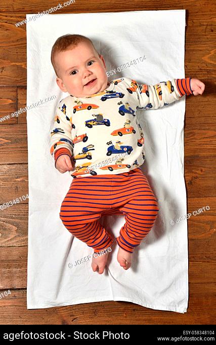 high angle view of a baby on the parquet floor dressed, looking at camera and smiling