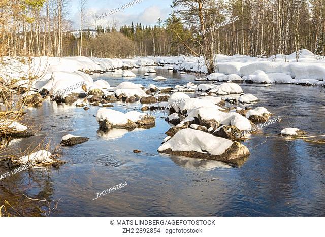 Creek with open water with ice and snow and the sky reflecting in the water, snow on the trees and on the rocks in the water, Norrbotten, Sweden