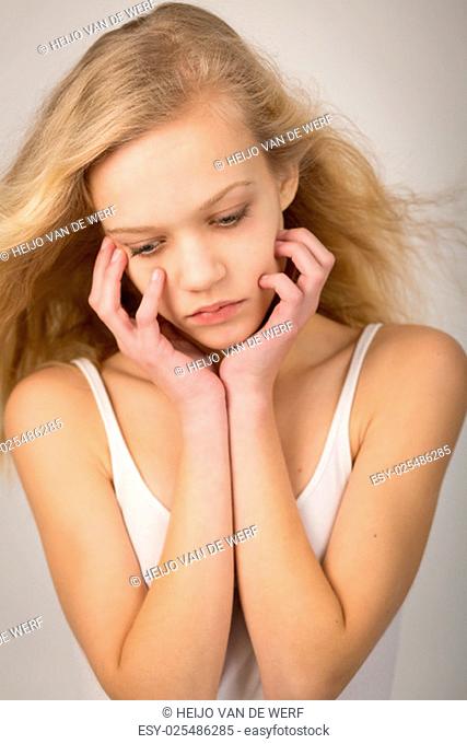 Studio shot of a beautiful teenage girl with long hair blowing in the wind with her hands on her face looking down