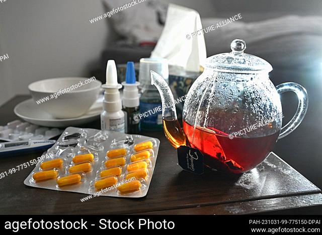ILLUSTRATION - 29 October 2023, Baden-Württemberg, Stuttgart: Medicines and a pot and cup of tea to fight a cold are placed on a bedside table