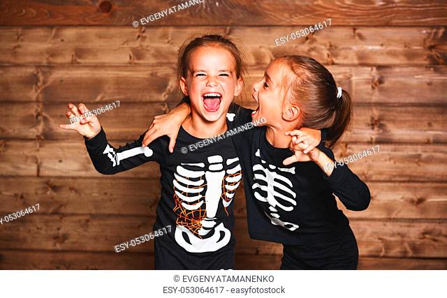 holiday halloween. funny funny sisters twins children in carnival costumes skeleton on a wooden background