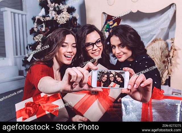 Beautiful girl photographed themselves on the phone on the background of Christmas gifts. Decorative vintage apartment