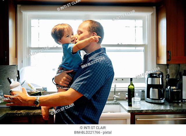 Father kissing baby son in kitchen