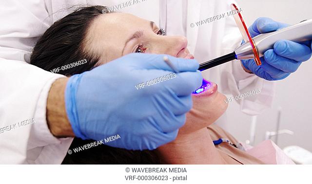 Dentist examining female patient with dental curing light
