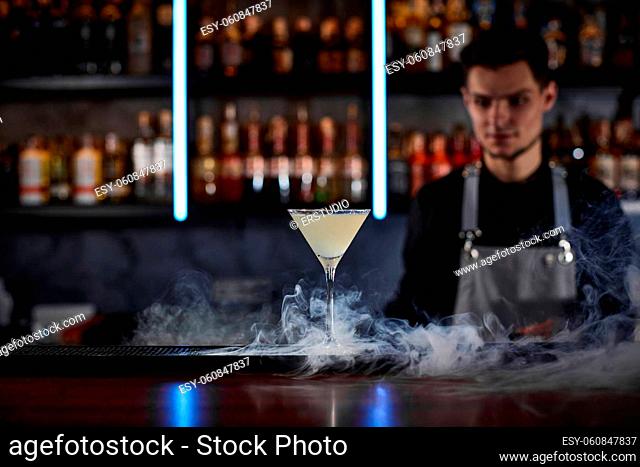 alcoholic cocktail with smoke on the bar table and barman on background