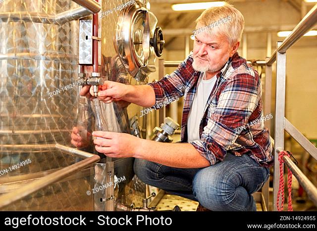 Winzer kontrolliert frischen Wein am Gärtank in einer Weinkellerei bei der Weinherstellung