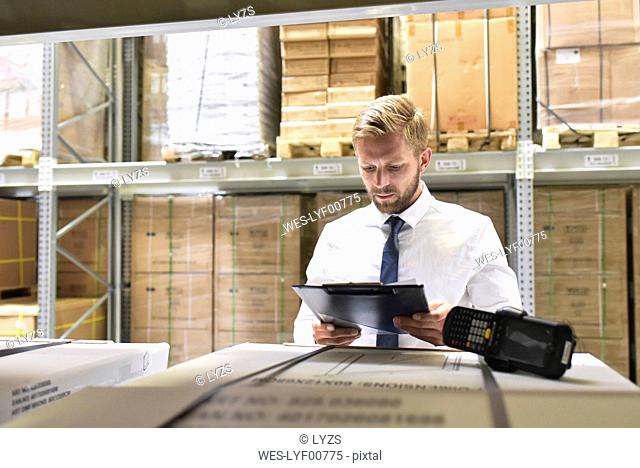 Businessman with clipboard and barcode scanner in warehouse